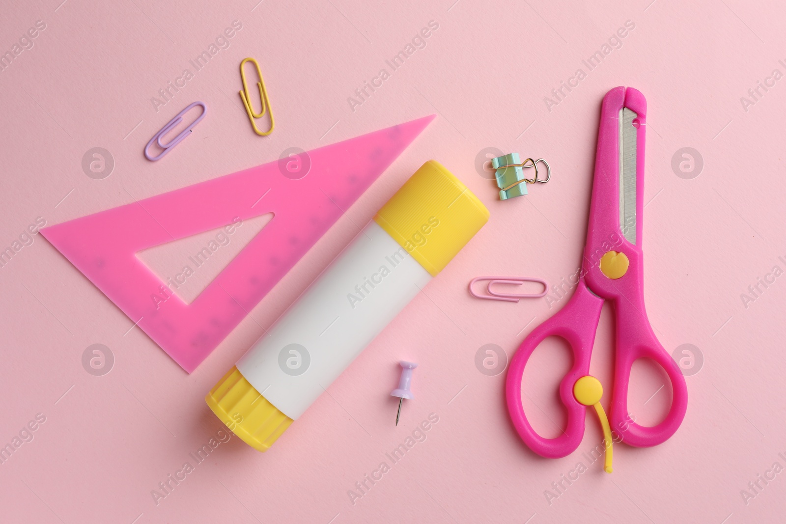 Photo of Glue stick, ruler, scissors and paper clips on pink background, flat lay