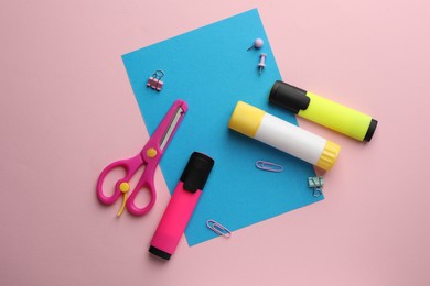 Photo of Glue stick, scissors, highlighters and blue sheet of paper on pink background, flat lay