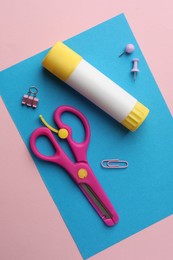 Photo of Glue stick, scissors and blue sheet of paper on pink background, flat lay