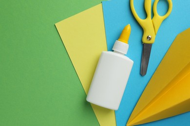 Photo of Glue in bottle, scissors, color paper and handmade plane on green background, flat lay. Space for text