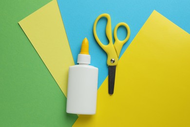 Photo of Glue in bottle, scissors and color paper on green background, flat lay