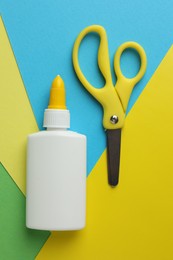 Photo of Glue in bottle, scissors and color paper on green background, flat lay