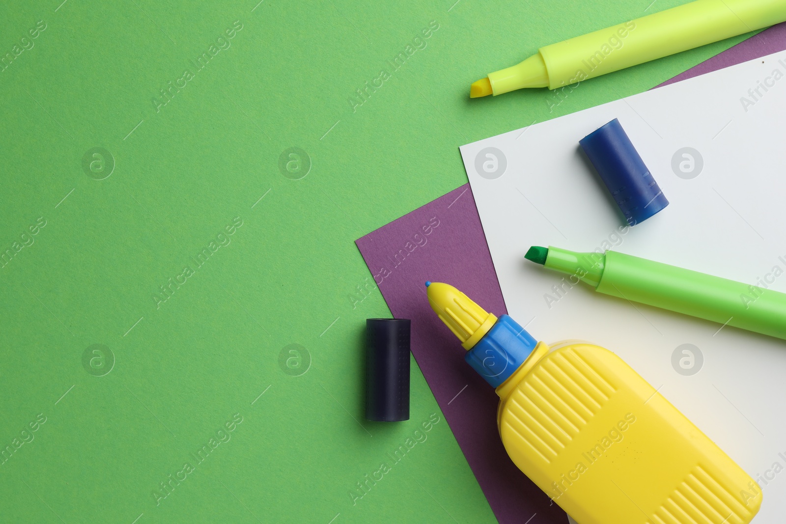 Photo of Glue in bottle, felt pens and color paper on green background, flat lay. Space for text