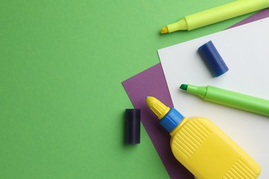 Photo of Glue in bottle, felt pens and color paper on green background, flat lay. Space for text