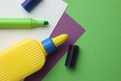 Photo of Glue in bottle, felt pen and color paper on green background, flat lay. Space for text