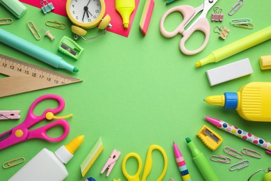 Photo of Frame of glue in bottles, alarm clock and other stationery on green background, flat lay. Space for text