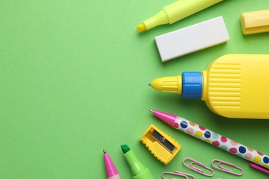 Photo of Glue in bottle and other stationery on green background, flat lay. Space for text