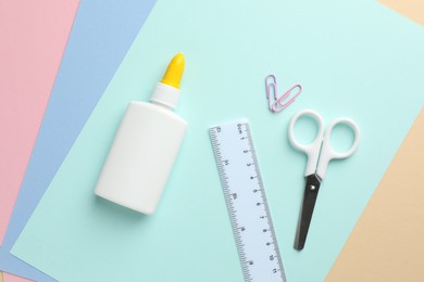 Photo of Glue in bottle, ruler and scissors on color paper, flat lay