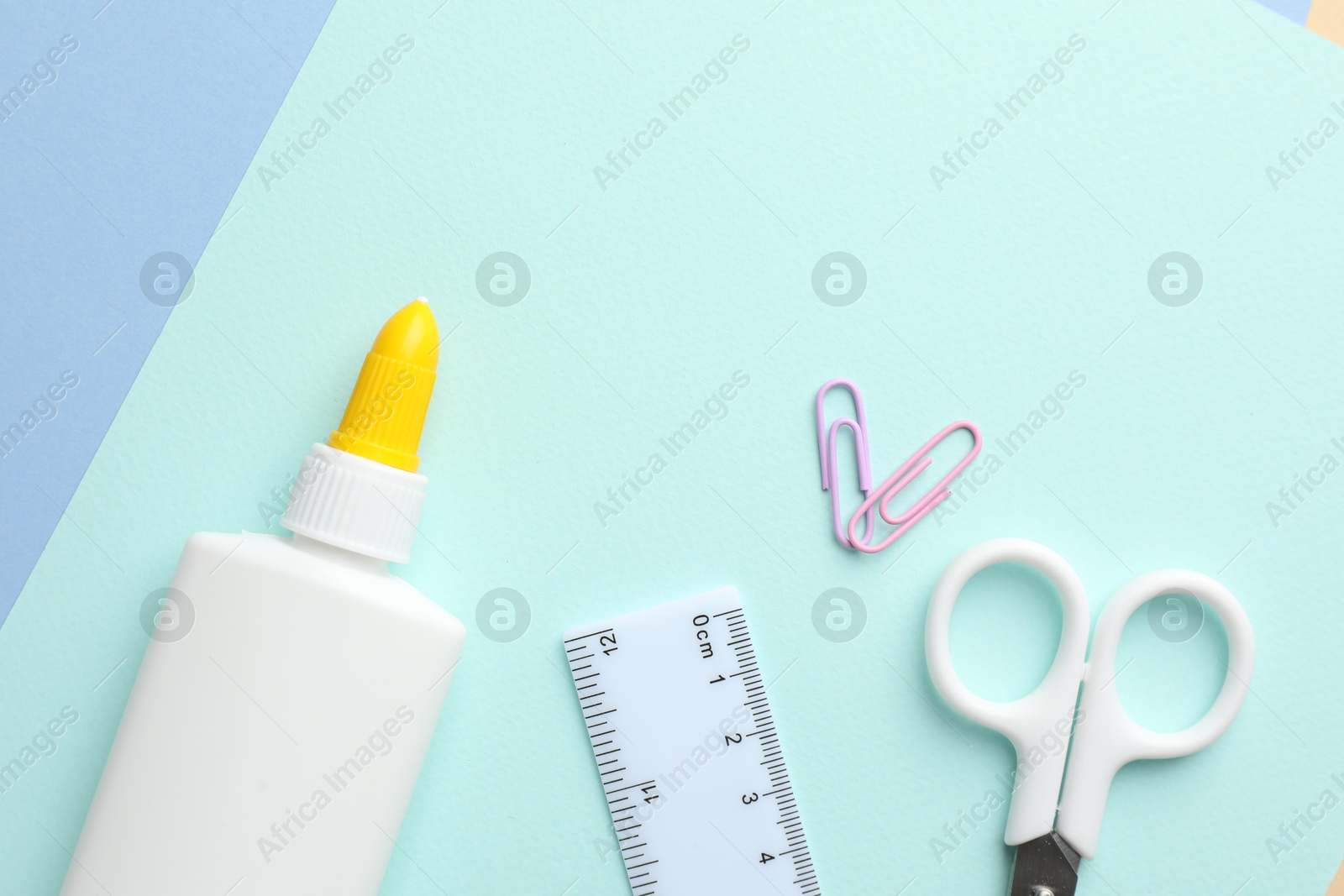 Photo of Glue in bottle, ruler and scissors on color paper, flat lay. Space for text