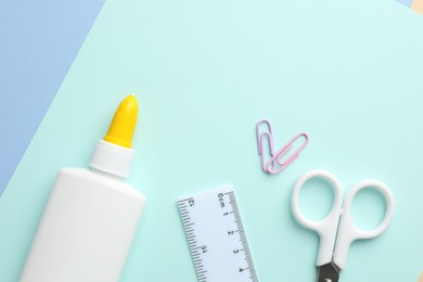 Photo of Glue in bottle, ruler and scissors on color paper, flat lay. Space for text