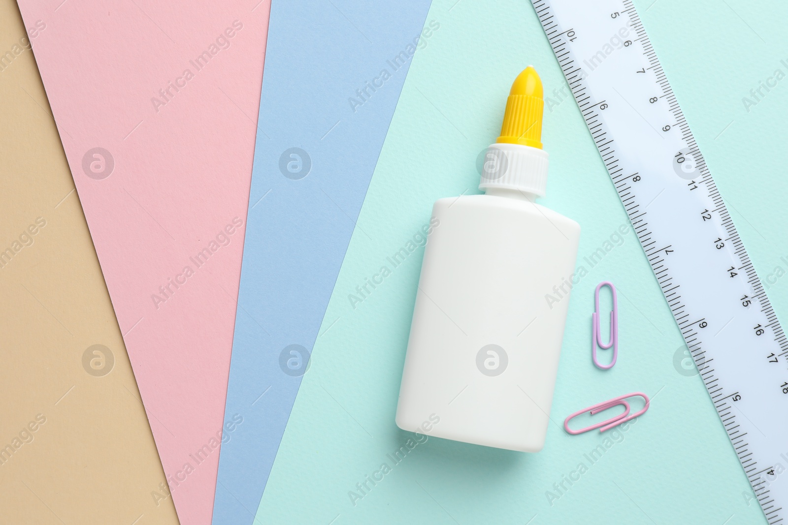 Photo of Glue in bottle, ruler and paper clips on color paper, flat lay. Space for text