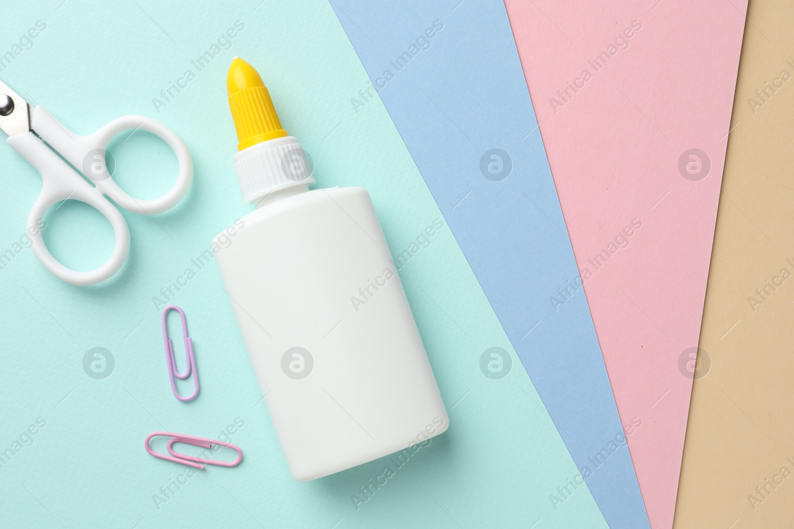 Photo of Glue in bottle, scissors and paper clips on color paper, flat lay. Space for text