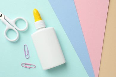 Photo of Glue in bottle, scissors and paper clips on color paper, flat lay. Space for text