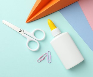Photo of Glue in bottle, scissors, handmade plane and paper clips on color paper, flat lay