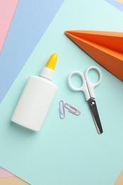 Photo of Glue in bottle, scissors, handmade plane and paper clips on color paper, flat lay