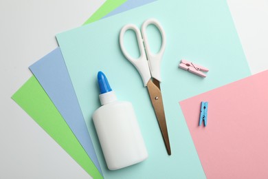 Photo of Glue, scissors, clips and color paper on white background, flat lay