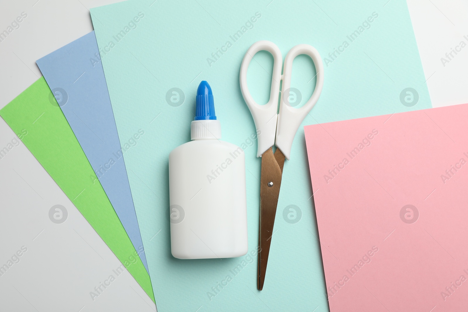 Photo of Glue, scissors and color paper on white background, flat lay