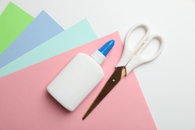 Photo of Glue, scissors and color paper on white background, flat lay