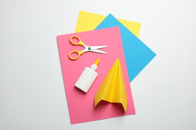 Photo of Glue, scissors, handmade plane and color paper on white background, flat lay