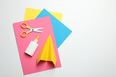 Photo of Glue, scissors, handmade plane and color paper on white background, flat lay. Space for text