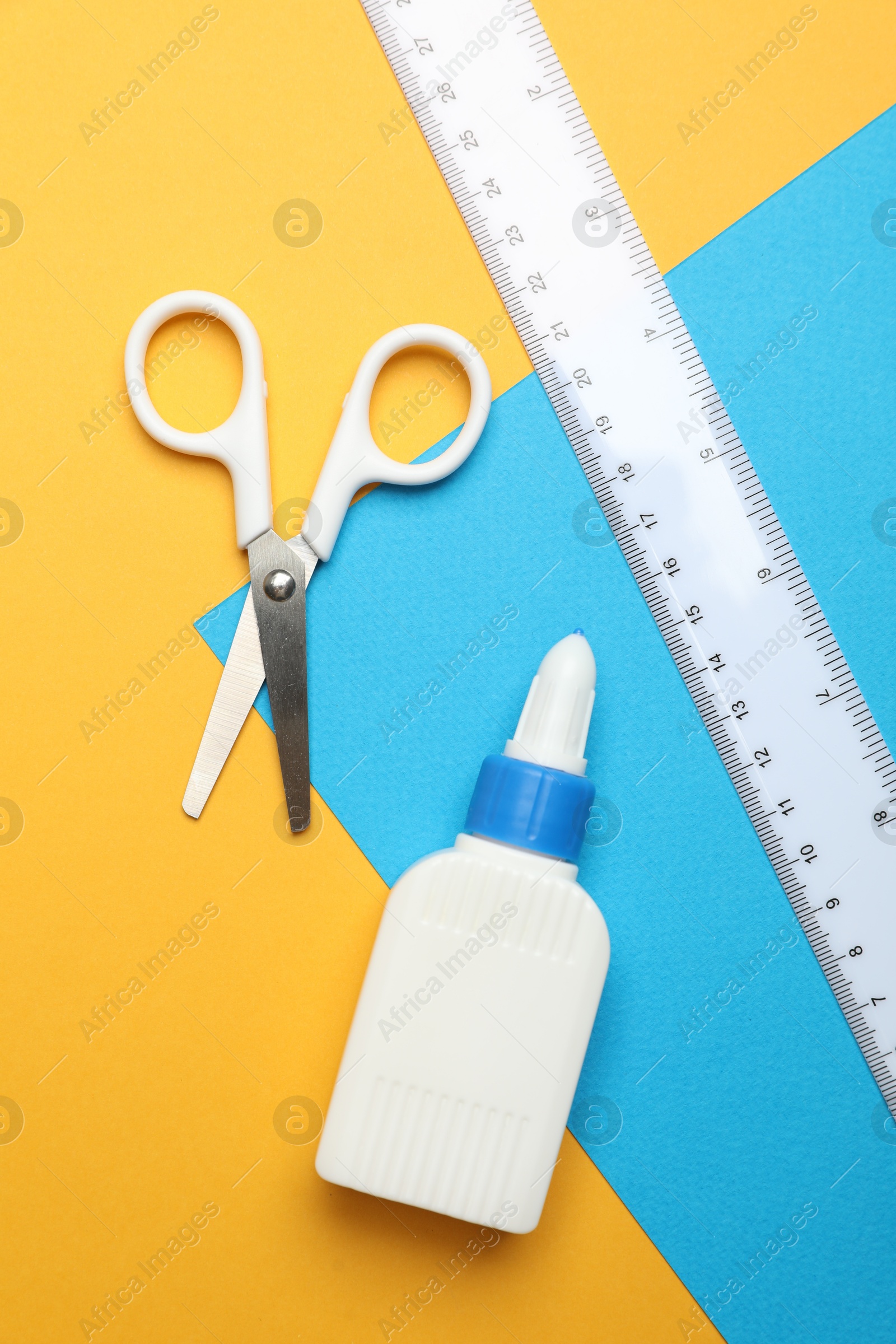 Photo of Glue, scissors, ruler and color paper on yellow background, flat lay