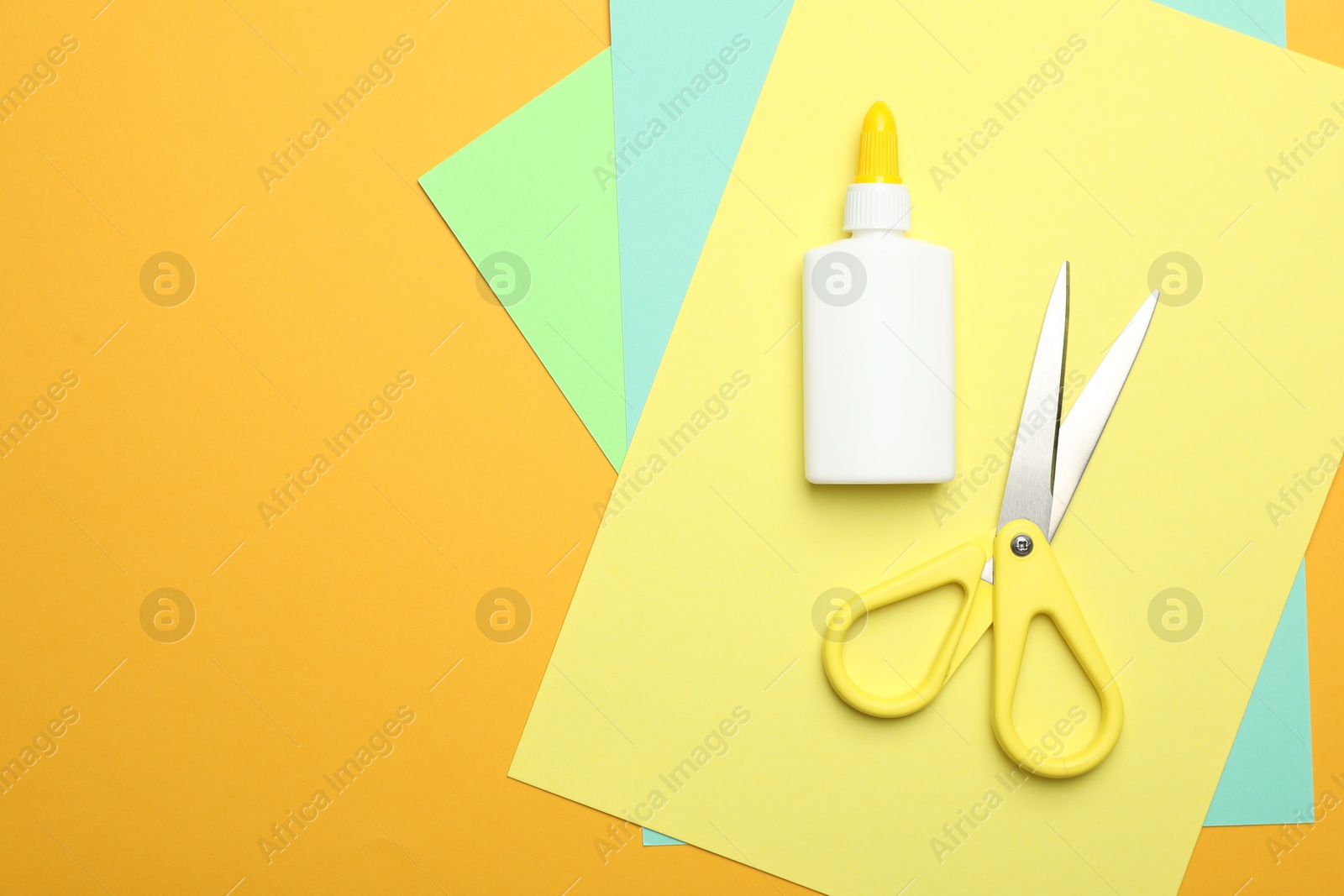 Photo of Glue, scissors and color paper on yellow background, flat lay. Space for text