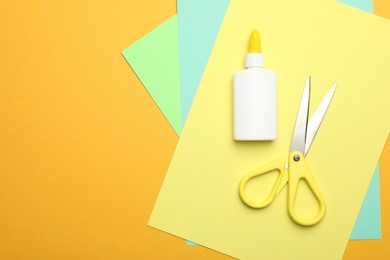 Photo of Glue, scissors and color paper on yellow background, flat lay. Space for text