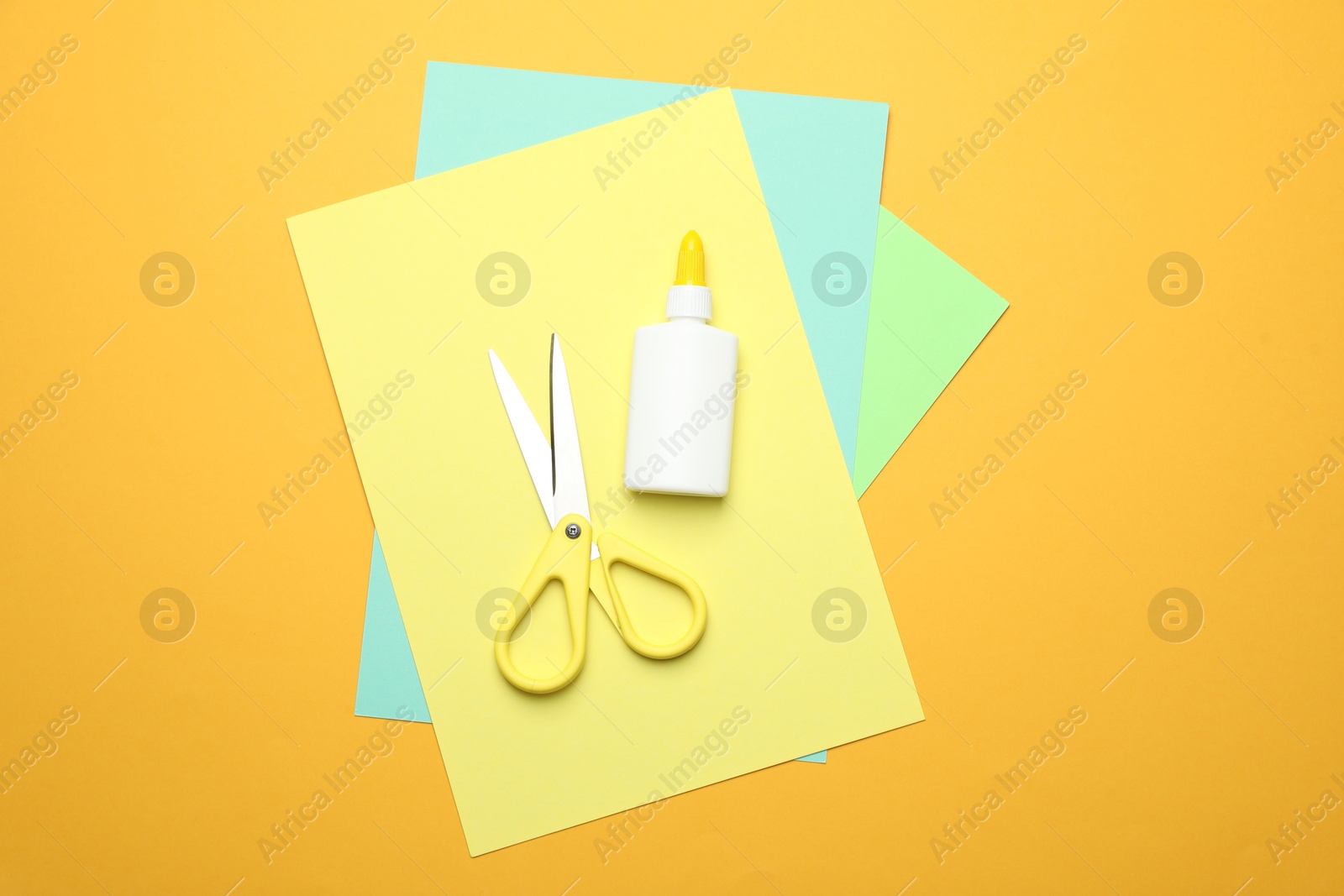 Photo of Glue, scissors and color paper on yellow background, flat lay