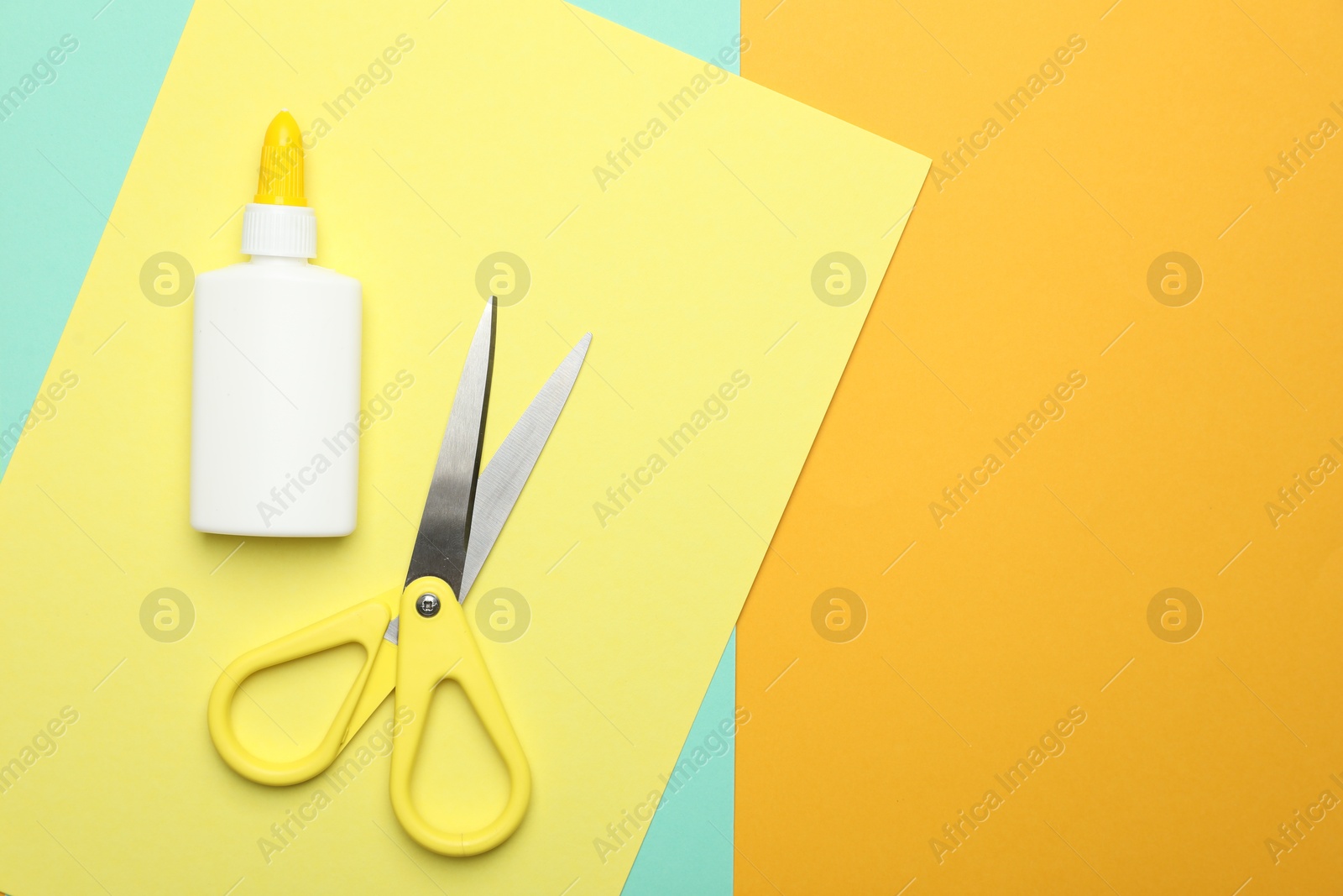 Photo of Glue, scissors and color paper on yellow background, flat lay. Space for text