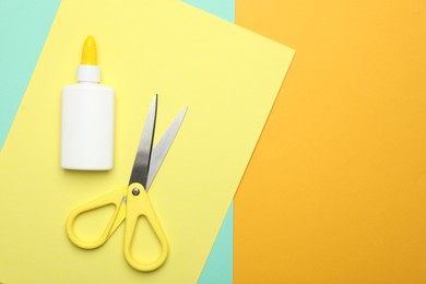 Photo of Glue, scissors and color paper on yellow background, flat lay. Space for text