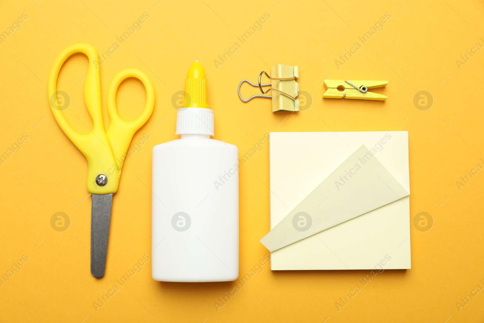 Photo of Glue and other stationery on yellow background, flat lay