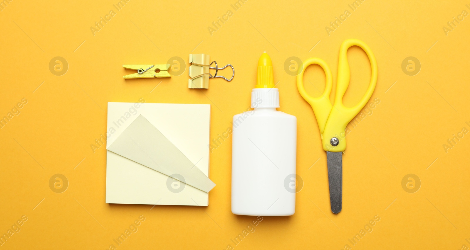 Photo of Glue and other stationery on yellow background, flat lay