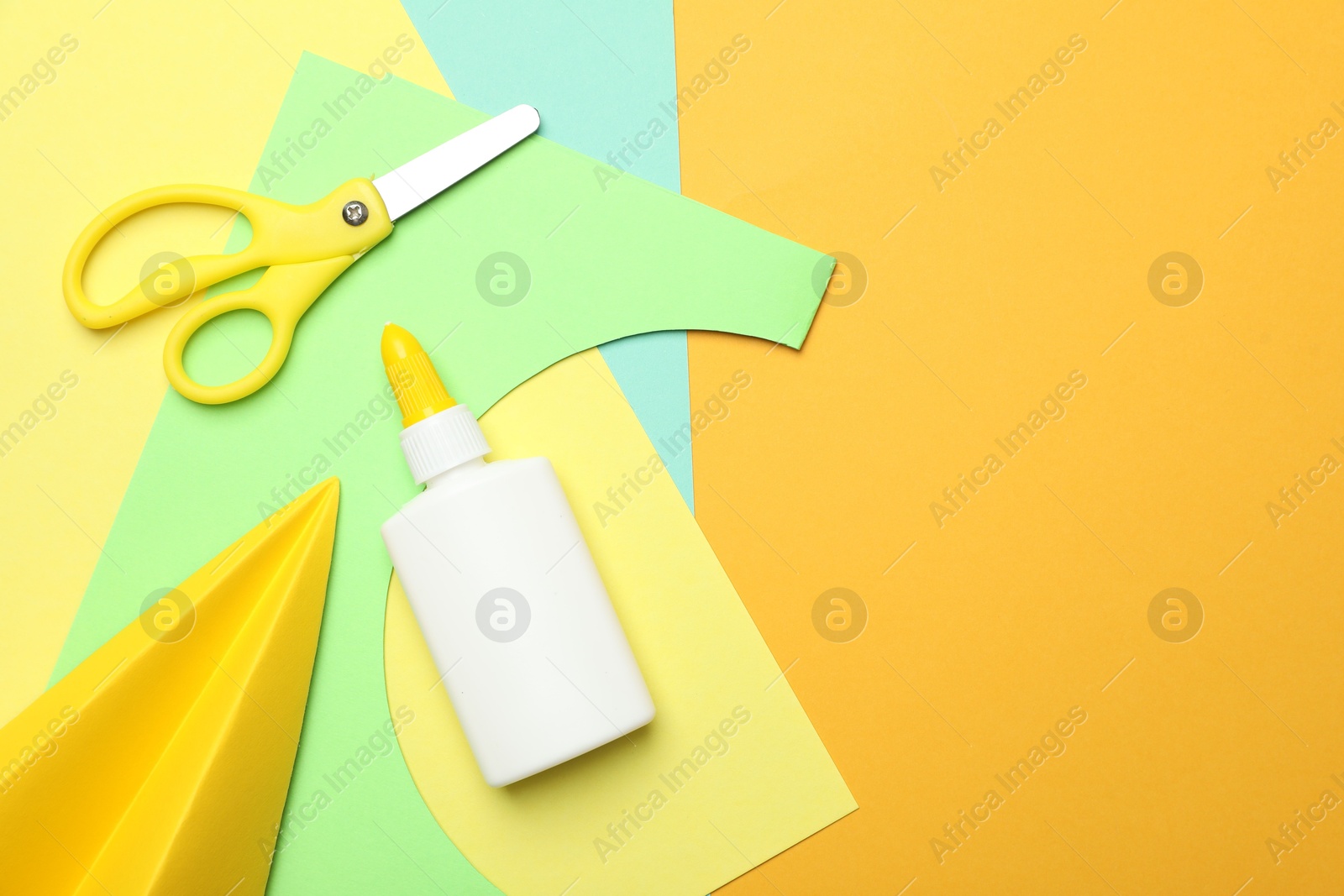 Photo of Glue, scissors, handmade plane and color paper on yellow background, flat lay. Space for text