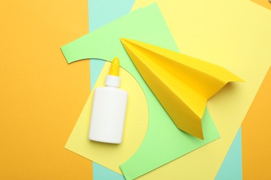 Photo of Glue, handmade plane and color paper on yellow background, flat lay