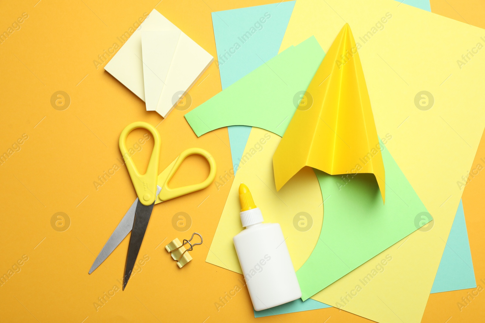 Photo of Glue and other stationery on yellow background, flat lay