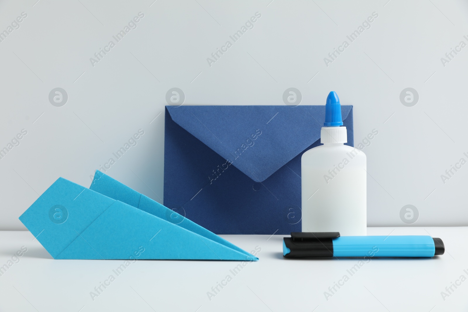 Photo of Glue, paper plane, highlighter and envelope on white table