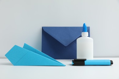 Photo of Glue, paper plane, highlighter and envelope on white table