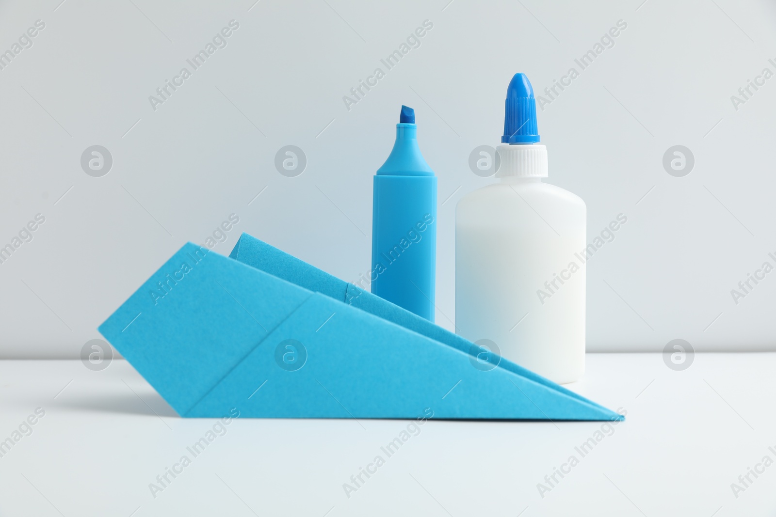 Photo of Glue, paper plane and highlighter on white table