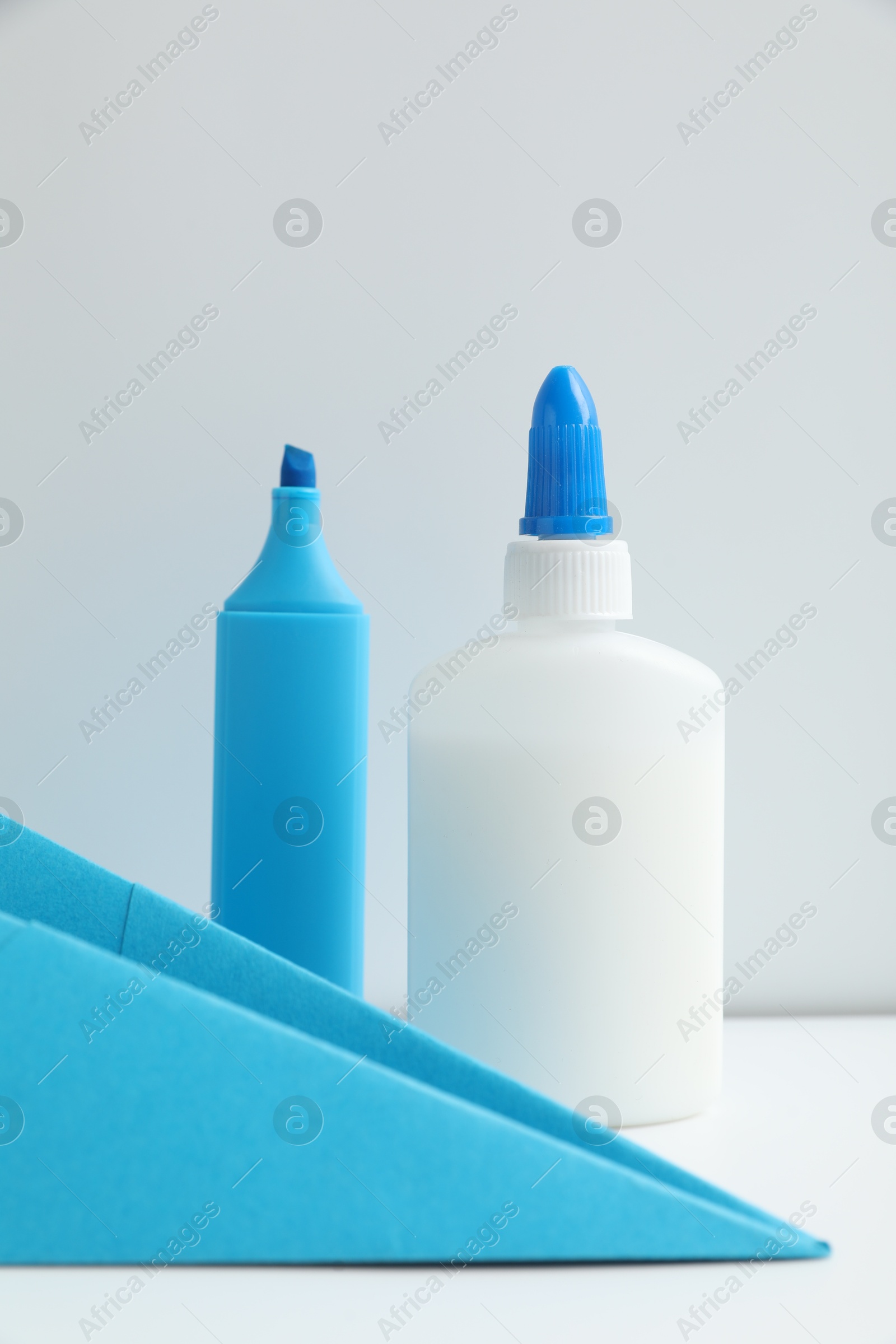 Photo of Glue, paper plane and highlighter on white table
