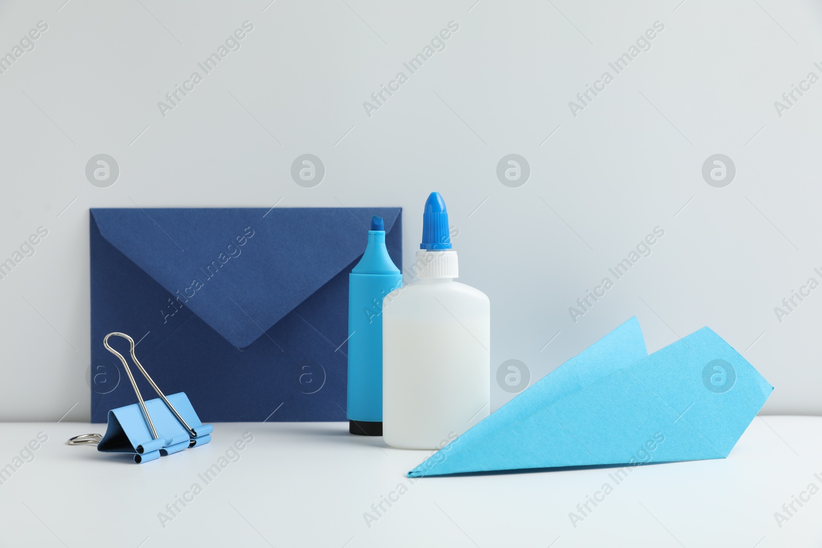 Photo of Glue, paper plane, highlighter, clip and envelope on white table. Space for text