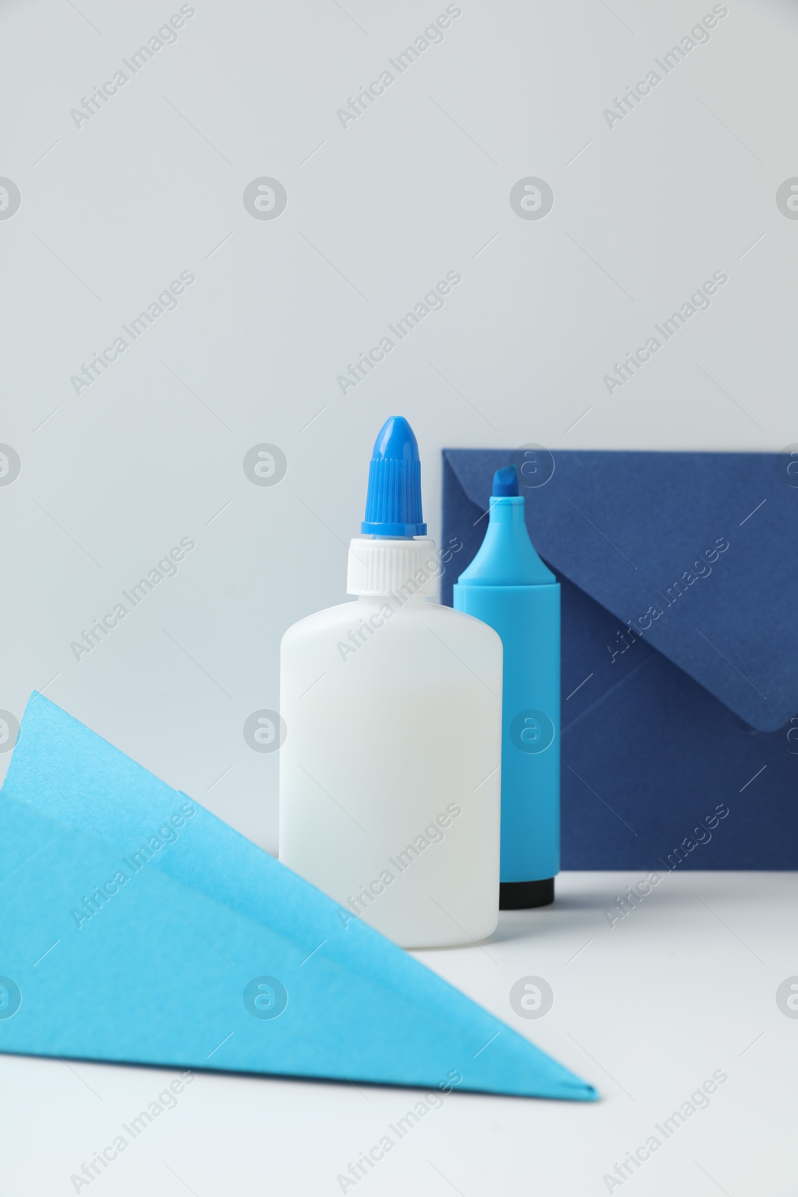 Photo of Glue, paper plane, highlighter and envelope on white table