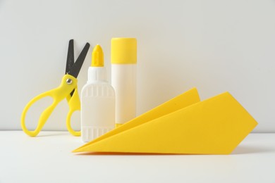 Photo of Liquid and stick glue, paper plane, scissors on white table