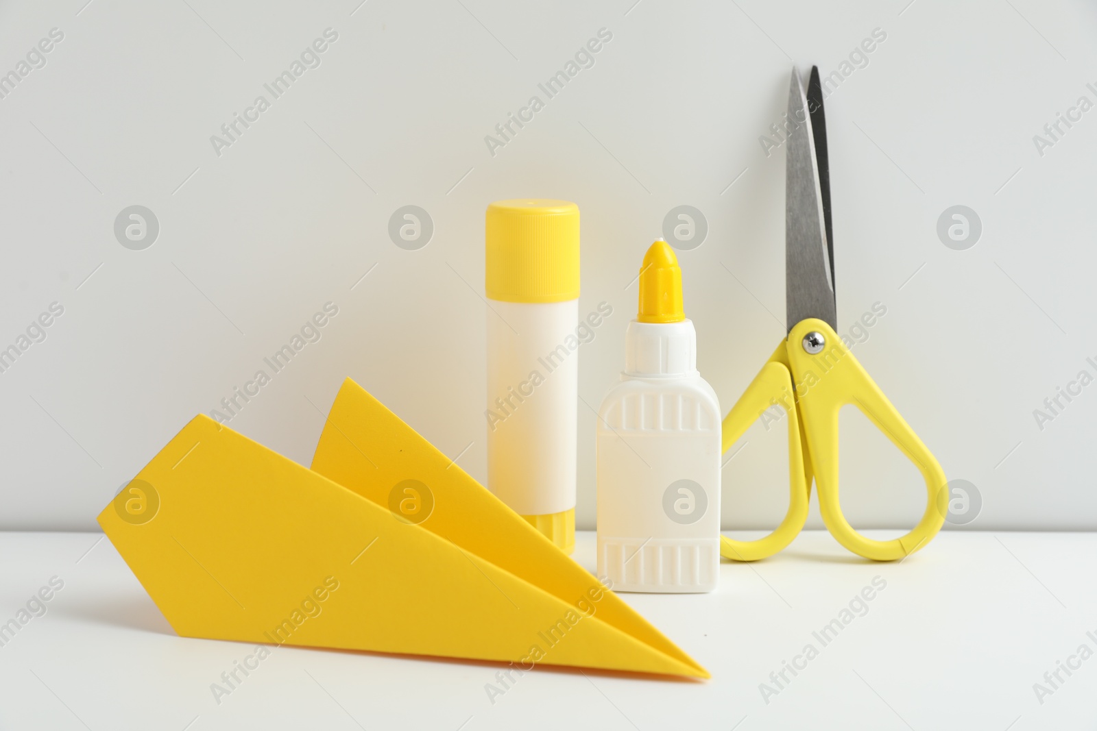 Photo of Liquid and stick glue, paper plane, scissors on white table