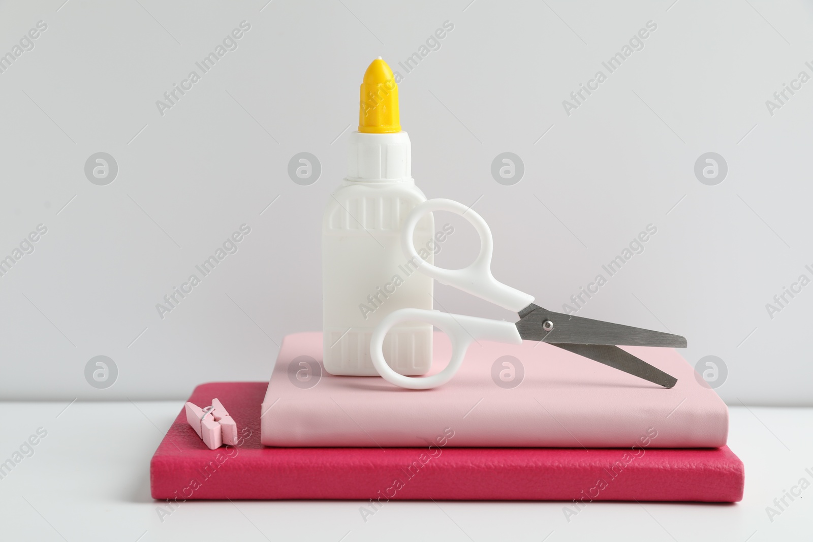 Photo of Glue, scissors, clip and notebooks on white table