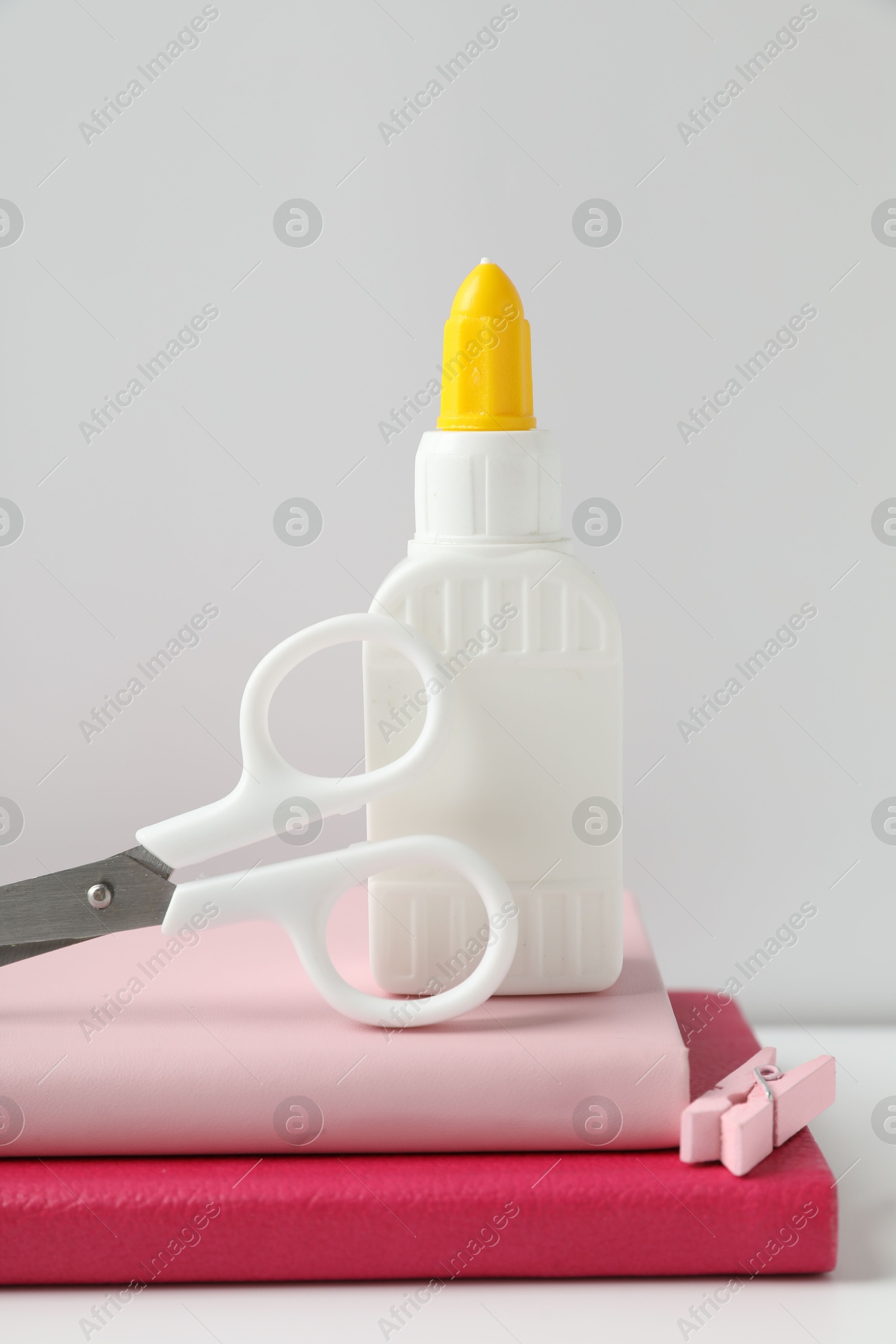 Photo of Glue, scissors, clip and notebooks on white table