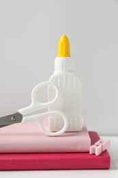Photo of Glue, scissors, clip and notebooks on white table