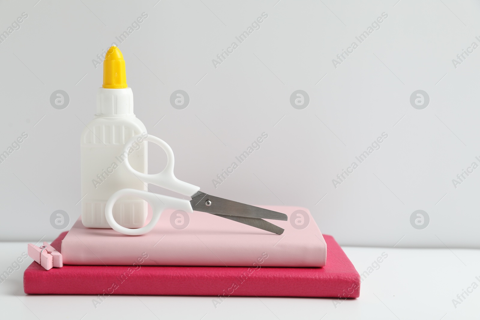 Photo of Glue, scissors, clip and notebooks on white table. Space for text