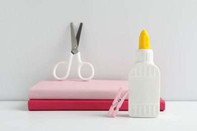 Photo of Glue, scissors, clip and notebooks on white table