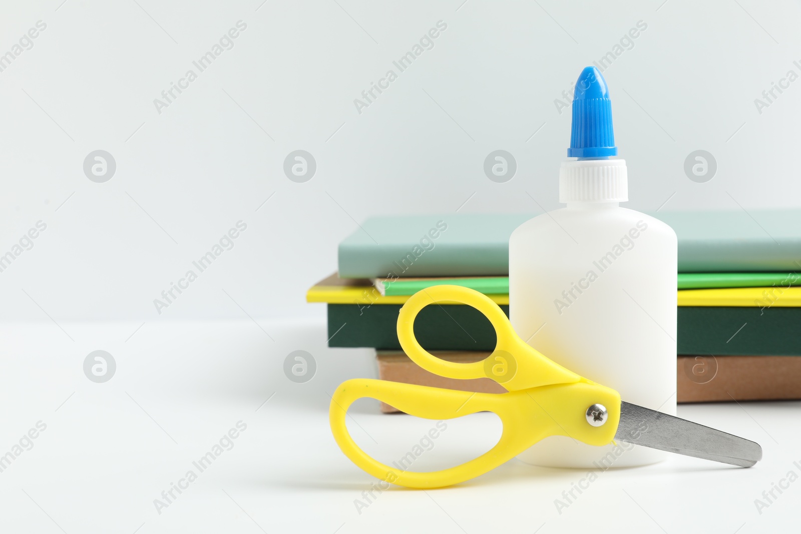 Photo of Glue, scissors and notebooks on white table. Space for text