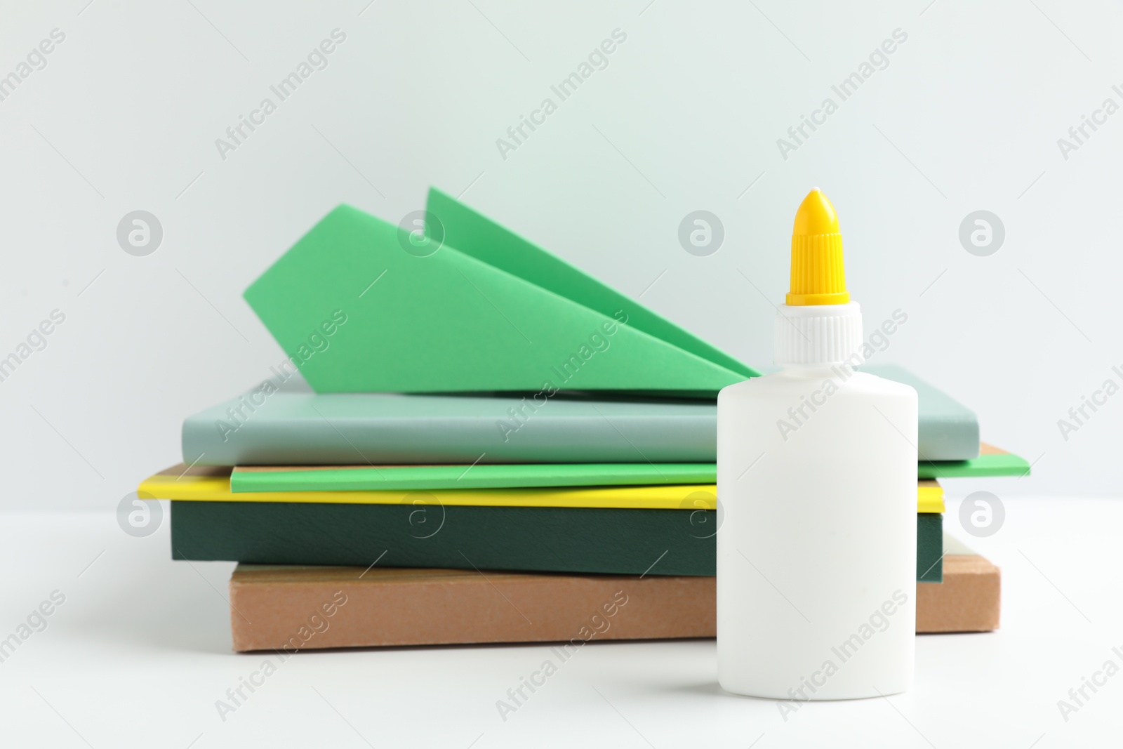 Photo of Glue, paper plane and notebooks on white table